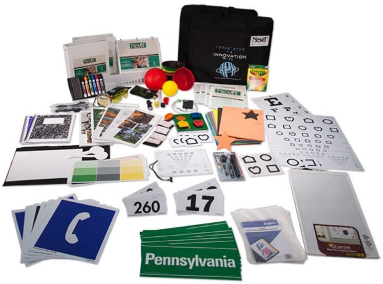 An assortment of low-vision assessment and training materials, including eye charts, colour and shape cards, number and symbol cards, small objects, printed activities, and carrying cases.