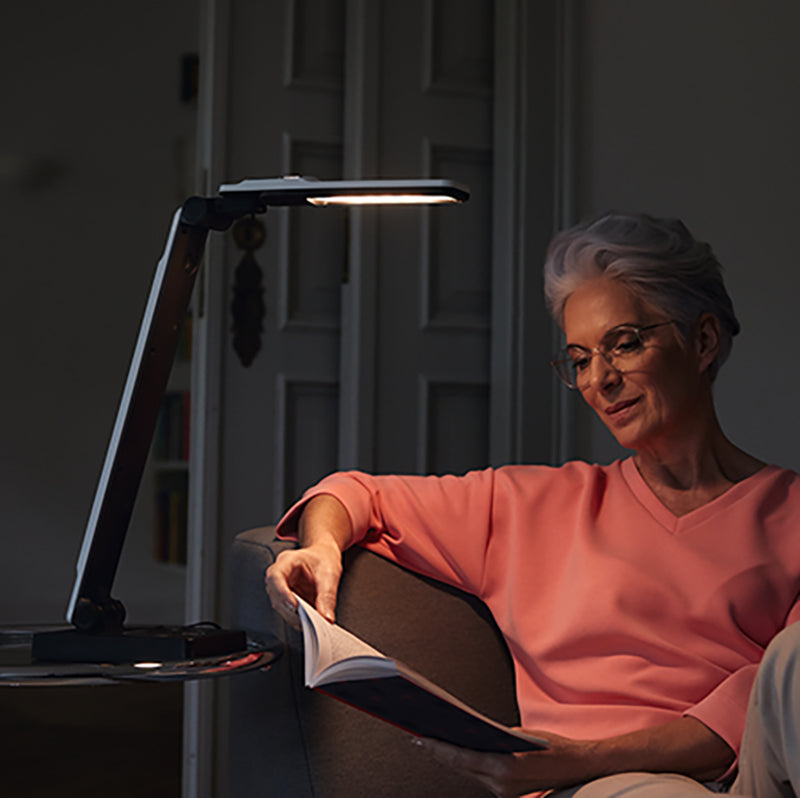 A user using the Elumentis Lamp on a side table to read a book.