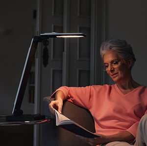 A user using the Elumentis Lamp on a side table to read a book.