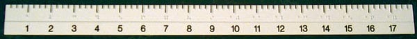 A close-up of a white plastic ruler with black printed numbers and measurement markings, spanning horizontally across the frame with Braille 