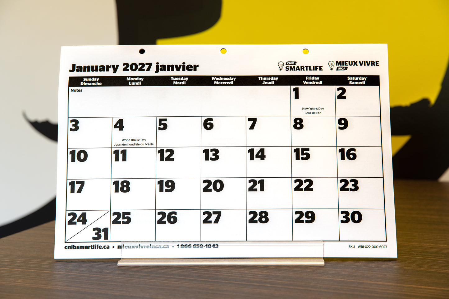 A 2027 CNIB SmartLife  calendar on a wooden surface, with a blurred yellow and black background.