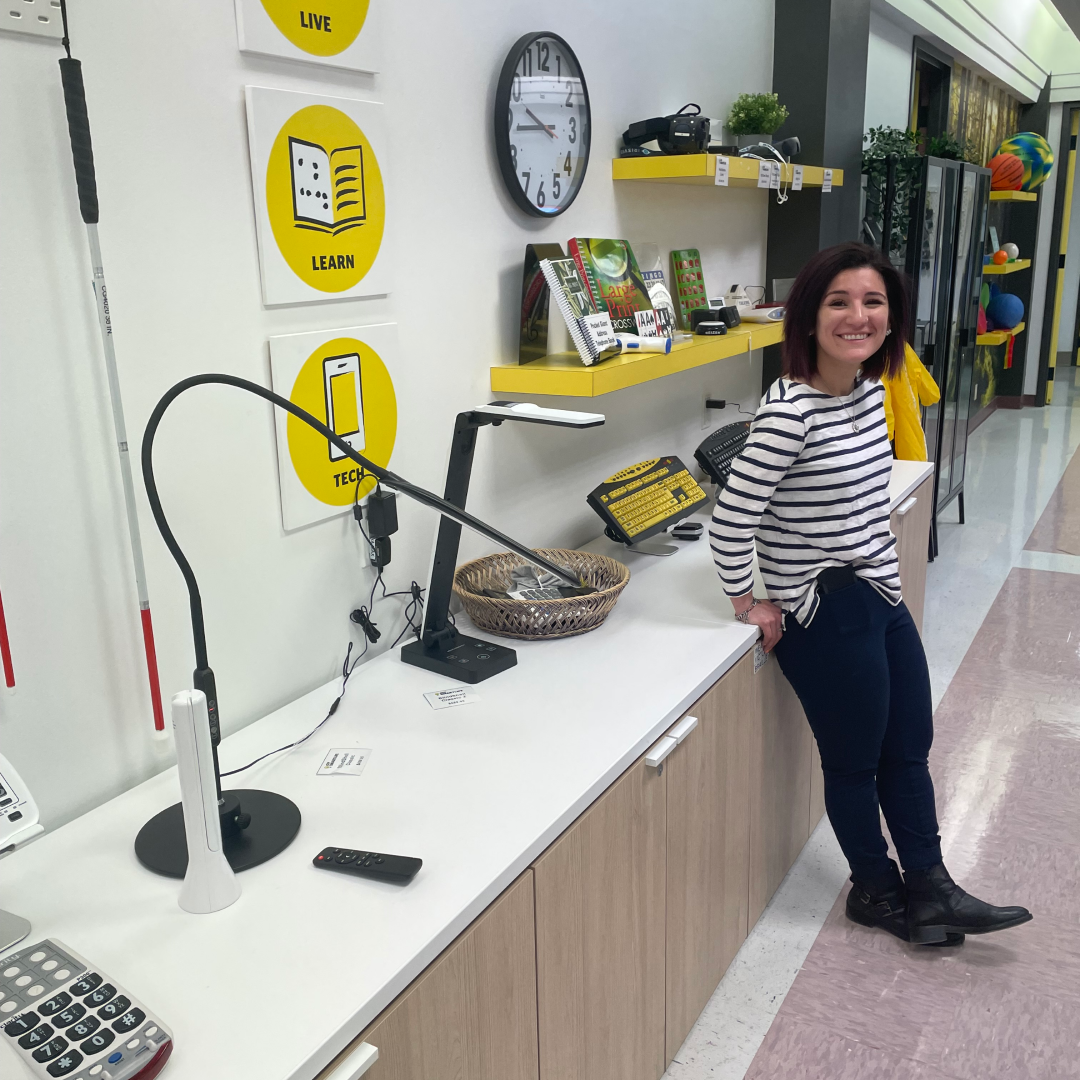 A smiling SmartLife Coach leans against a table that showcases various different types of technology. Un conseiller Mieux Vivre souriant est appuyé contre une table qui présente différents types de technologies.