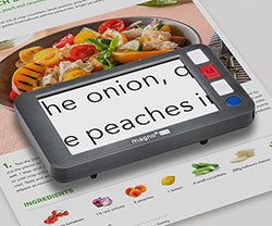 A digital magnifier with a black frame and four buttons sitting on a cookbook