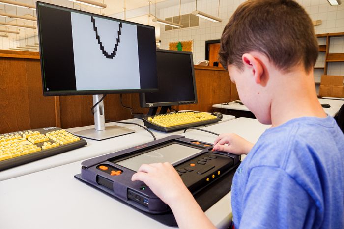 Student using Monarch tactile display in a classroom with a connected monitor showing visual content